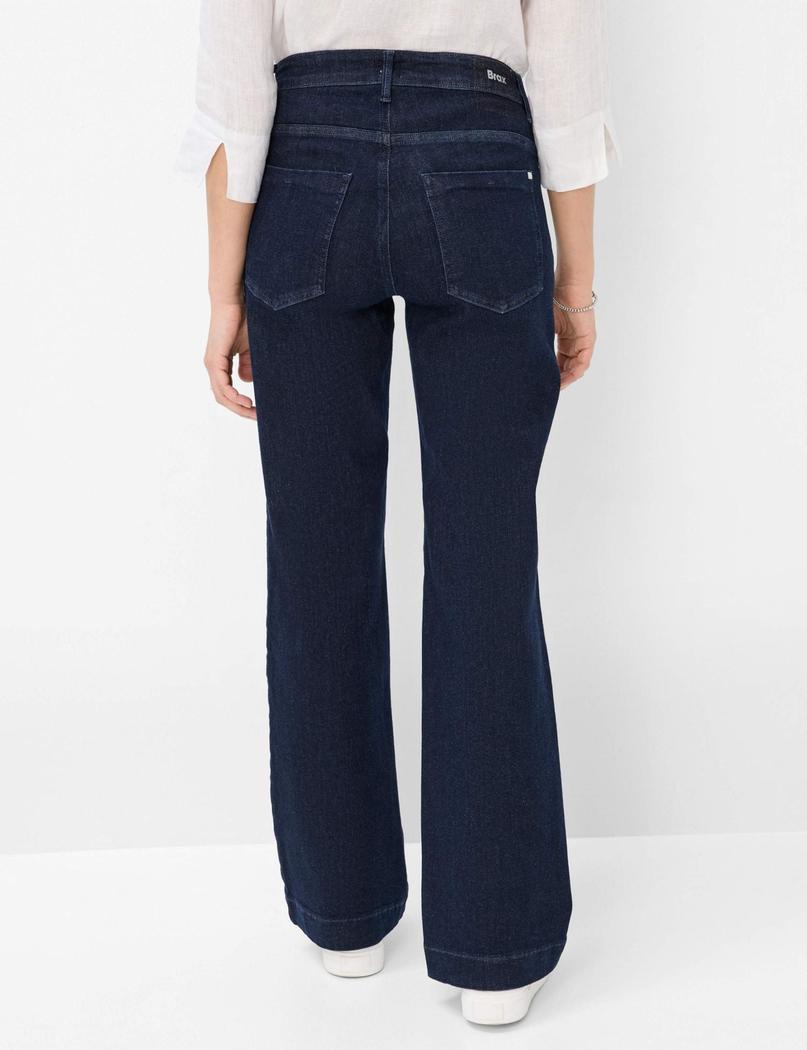 Baksiden av en person i mørkeblå jeans med vide ben og en hvit bluse.