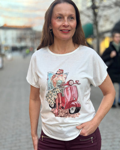 Kvinne med T-skjorte som viser en person på rød scooter med kart; teksten "Vespa" er synlig.