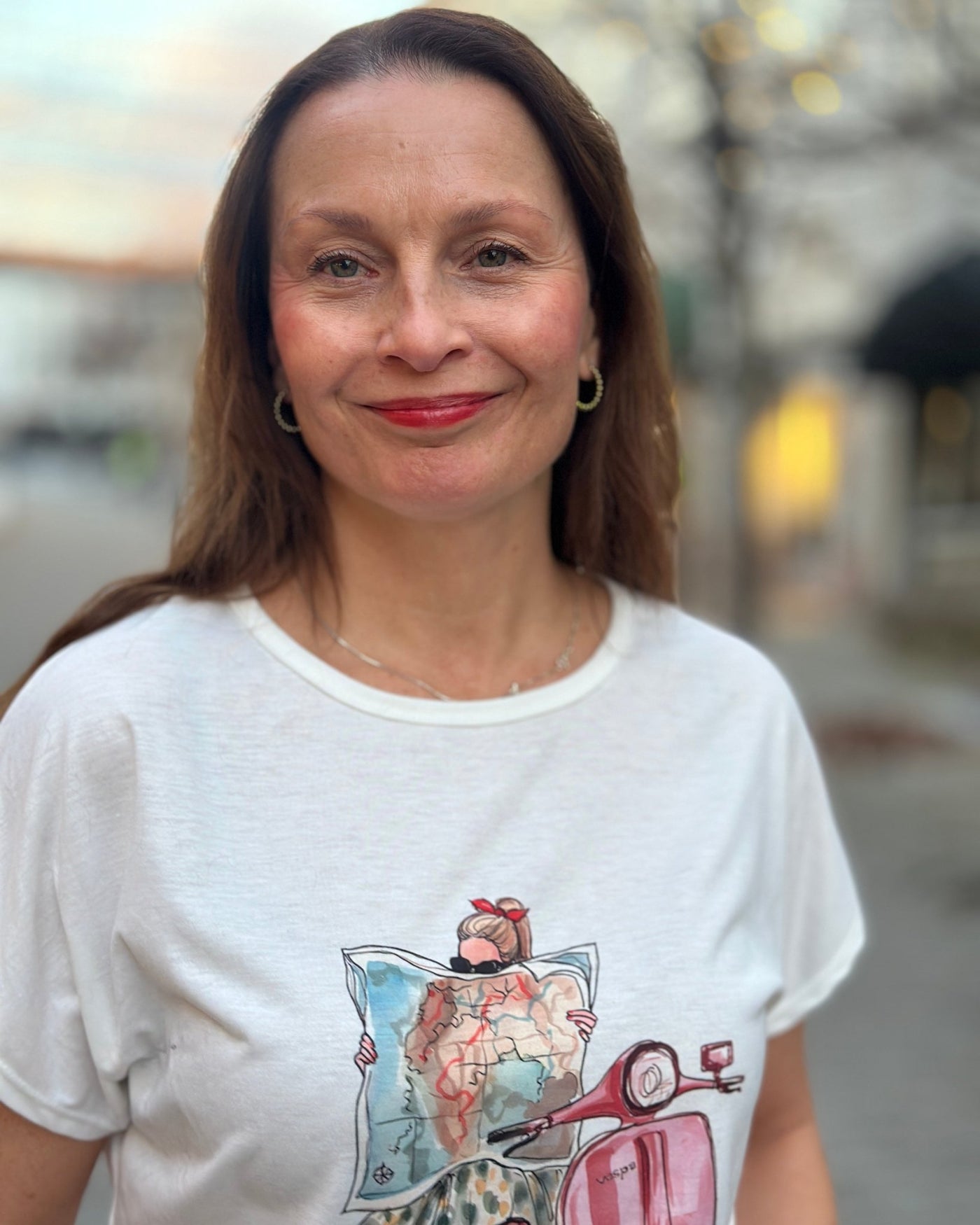 T-skjorte med trykk av en person på en rød scooter, leser et kart; teksten "Vespa" er synlig.