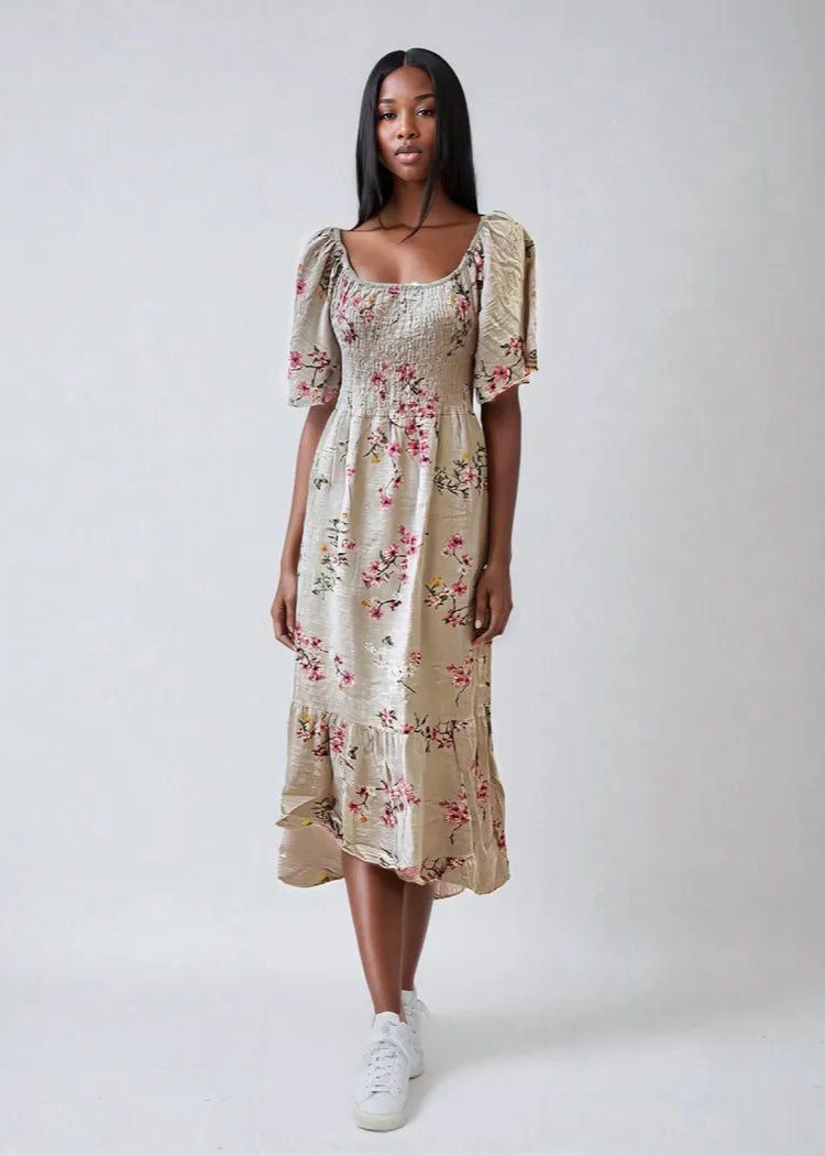 Kvinne i blomstret kjole med pufferm, volangkant og tettsittende bodice på lys beige bakgrunn.