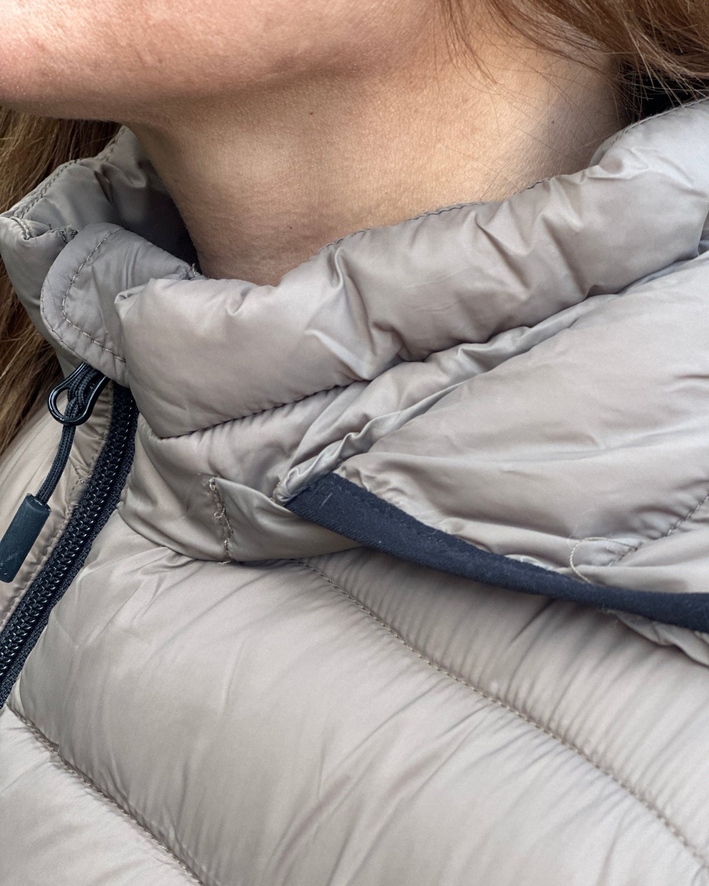Nærbilde av en quiltet jakke med høy krage og glidelås i beige stoff.