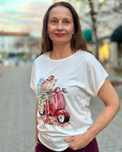 T-skjorte med trykk av en person på en rød scooter, leser et kart. "Vespa" står på scooteren.