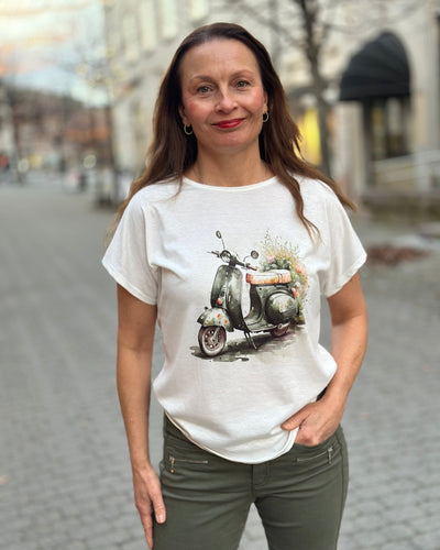 Kvinne med hvit T-skjorte med scooter- og blomstertrykk, løs passform og korte ermer.