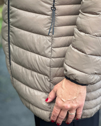 Beige quiltet jakke med glidelås, horisontale sømmer og en hånd med rødlakkerte negler.