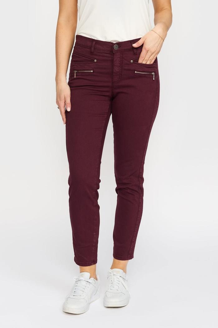 Burgunder slim-fit bukse med to glidelåslommer, hvit topp og hvite sneakers.