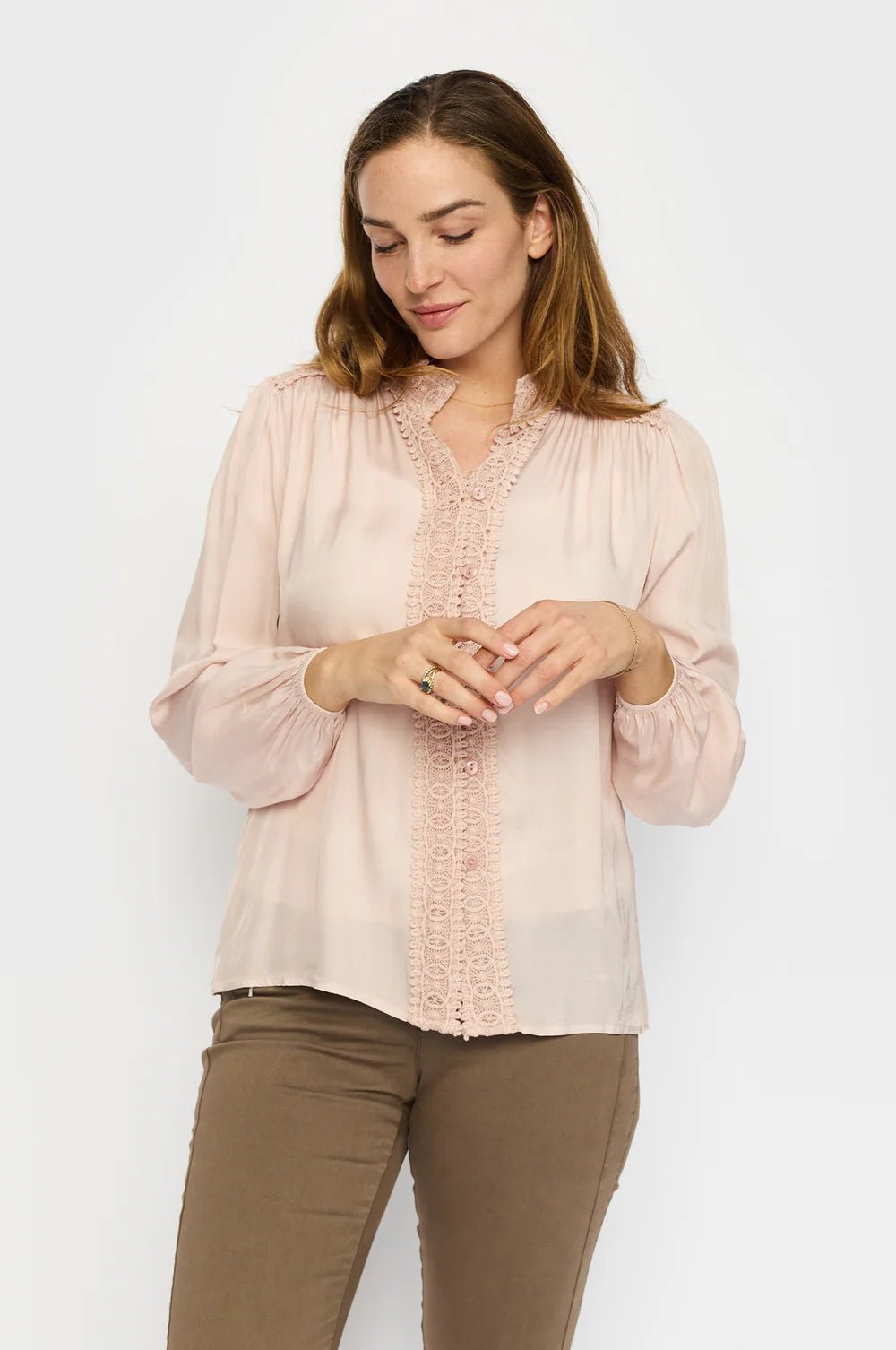 Kvinne i lys rosa bluse med blonder langs kragen, knapper foran og puffede ermer.