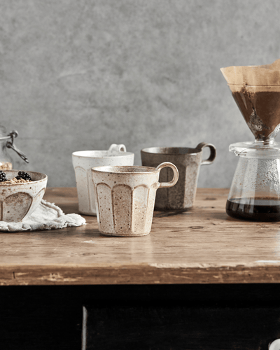 Tre krus i steintøy med flekkete mønster, i off-white, beige og grønn, på et rustikt trebord.