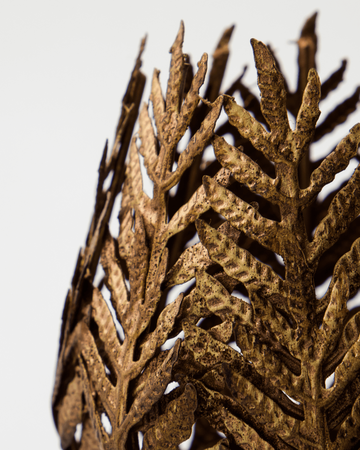 Nærbilde av gylden telysholder med intrikat bladlignende mønster og åpen struktur.