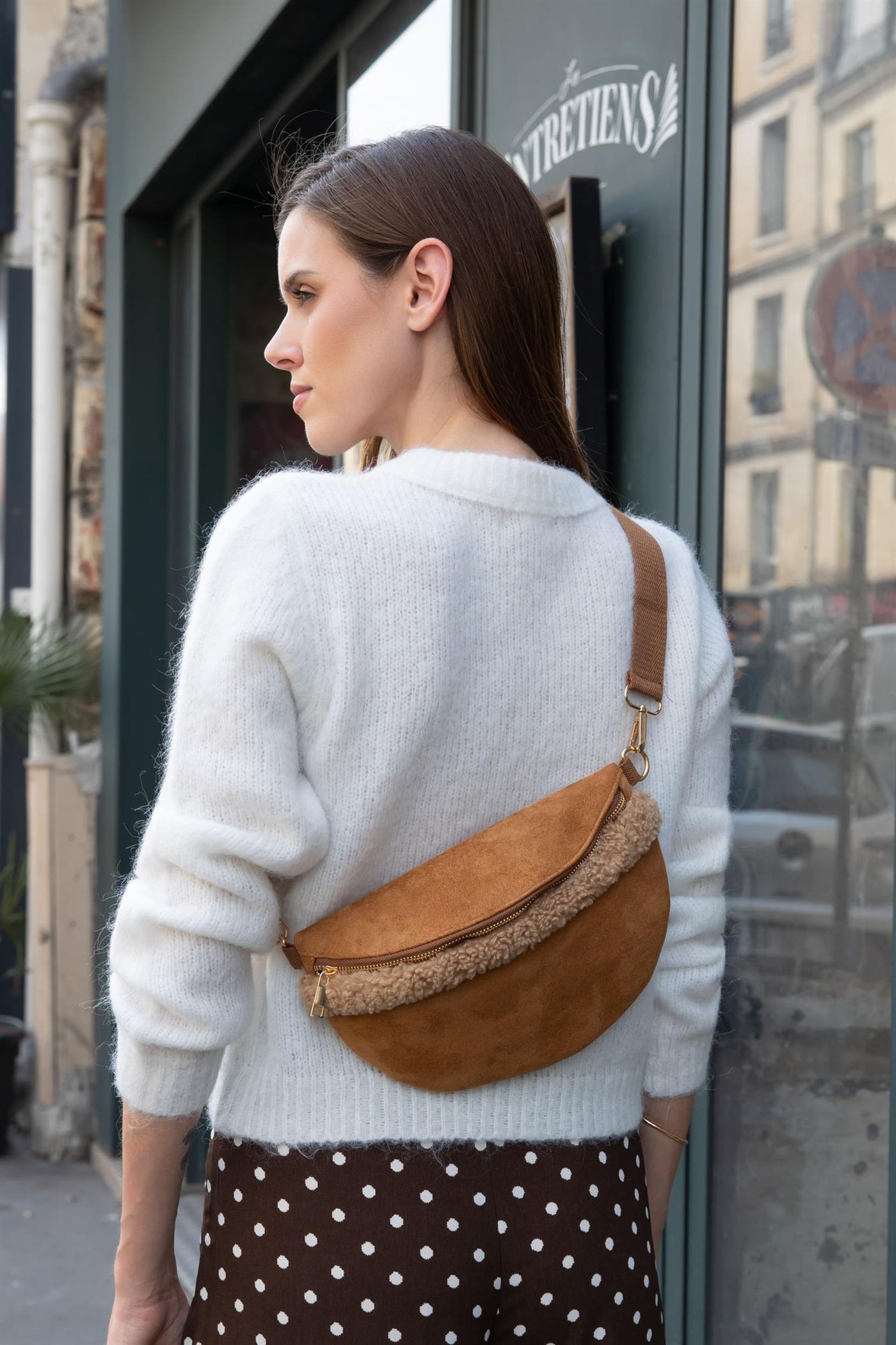 Kvinne i hvit genser med brun bum-bag med pelskant og justerbar stropp over skulderen.