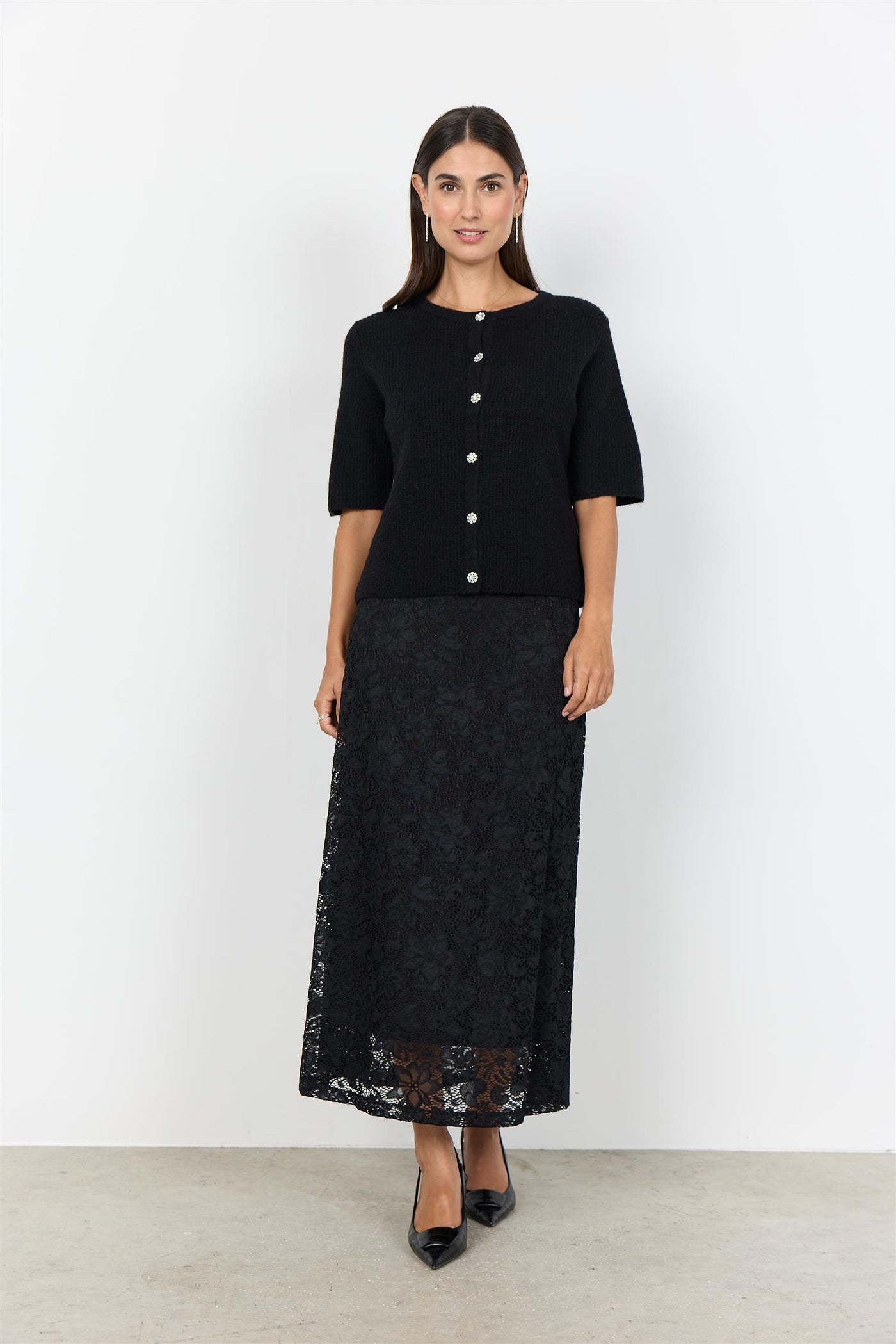 Sort plagg med korte ermer, strikket tekstur og blomsterformede dekorative knapper.
