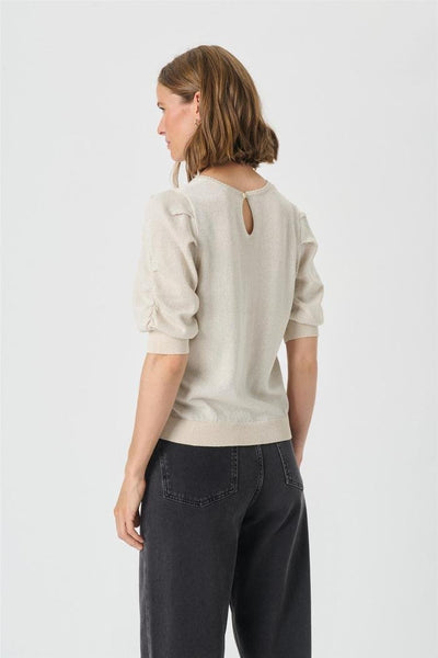 Lys genser med knapp bak, korte puffermer, rynker og ribbekant. Modellen har mørke jeans.