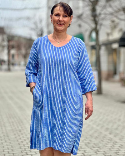 Blå- og hvitstripet kjole med 3/4-ermer og splitt, båret av kvinne i bymiljø.