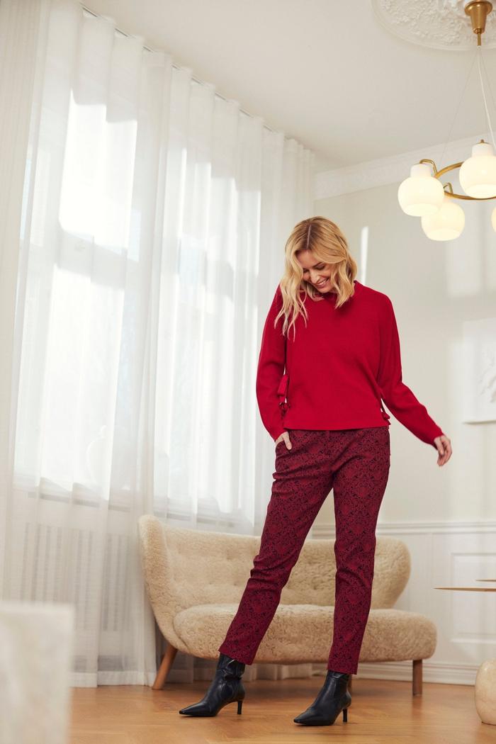 Person i mønstrede bukser med beltehemper, rød genser og svarte støvletter i lyst rom.