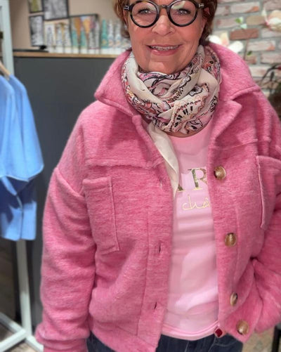 En person har på seg en rosa jakke med store knapper og et mønstret skjerf.