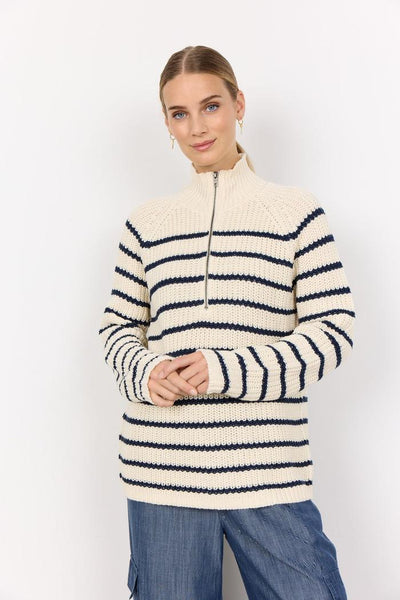 Person i strikket genser med mørke striper, høy krage med glidelås, iført jeans.