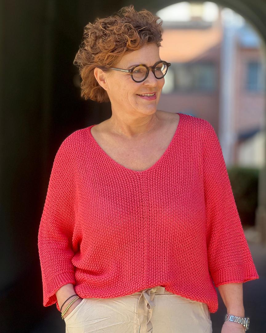 Person med rosa strikket genser med trekvart ermer, smilende i solskinn.